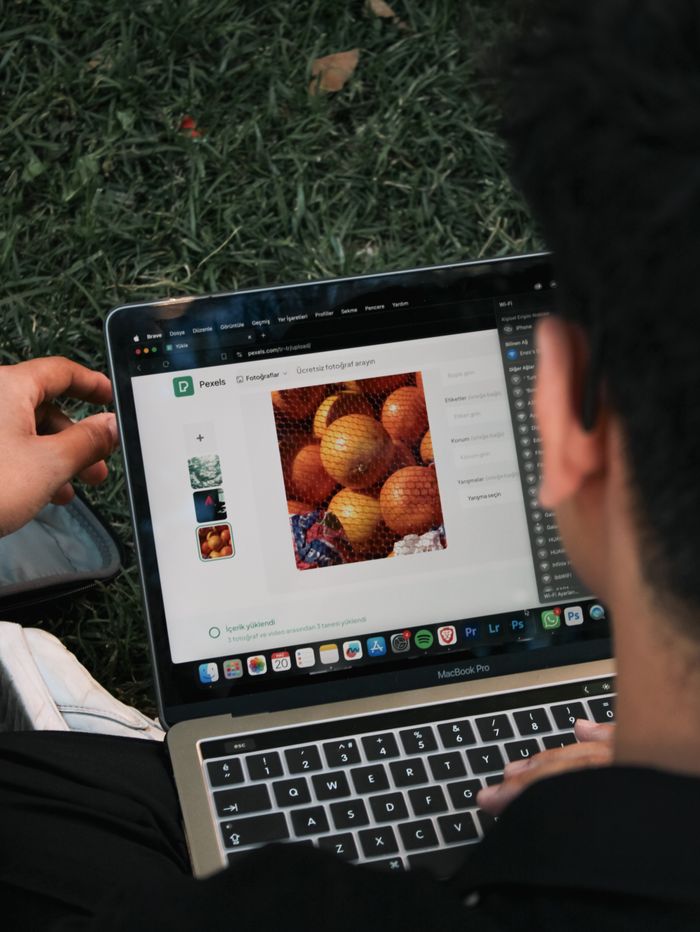 about-01 A man is editing a fruit photo on a MacBook Pro while seated outside on the grass.